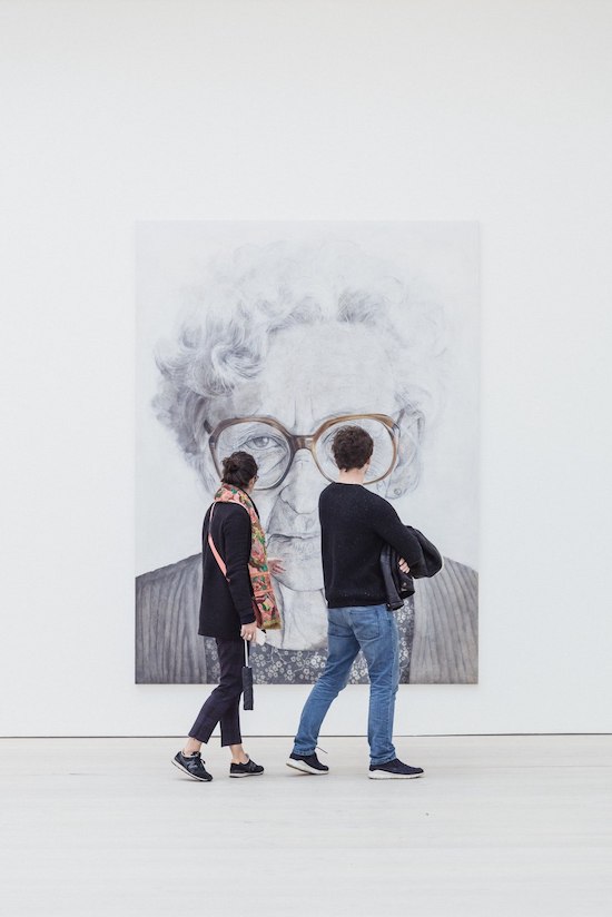 دو نفر در یک گالری عکس، در حال قدم زدن به نقاشی چهره‌ای از یک خانم مسن نگاه می‌کنند.